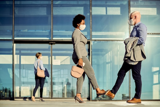 Collègues de travail avec des masques faciaux qui se cognent les pieds tout en saluant à l'extérieur