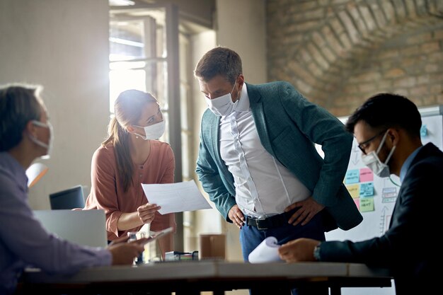 Collègues de travail avec masques de protection analysant les rapports d'une réunion au bureau