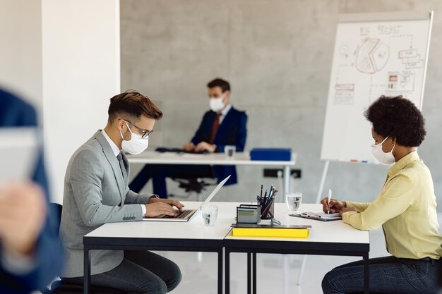 Collègues de travail portant des masques de protection lorsqu'ils travaillent au bureau