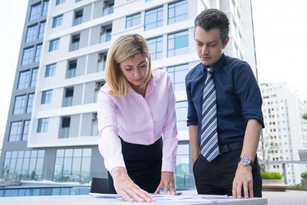 Collègues de travail réfléchi concentré debout près de table et analyse des documents