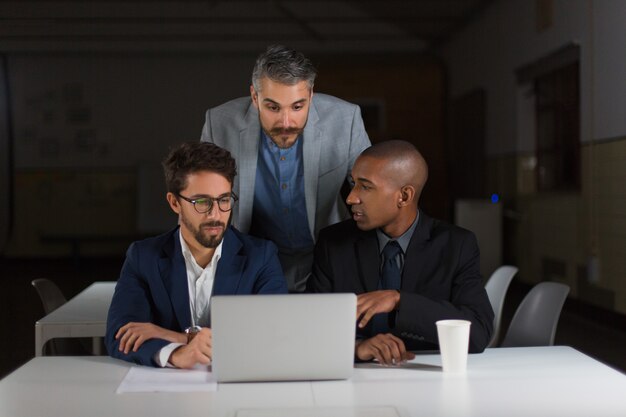 Collègues de travail utilisant un ordinateur portable dans un bureau sombre