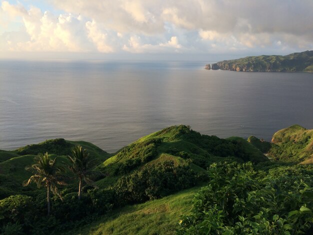 collines couvertes de vert par le corps de la mer sous un ciel nuageux