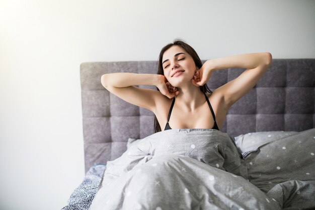 Commencer une nouvelle journée. Belle jeune femme en lingerie, gardant les mains dans les cheveux tout en étant assis sur le lit