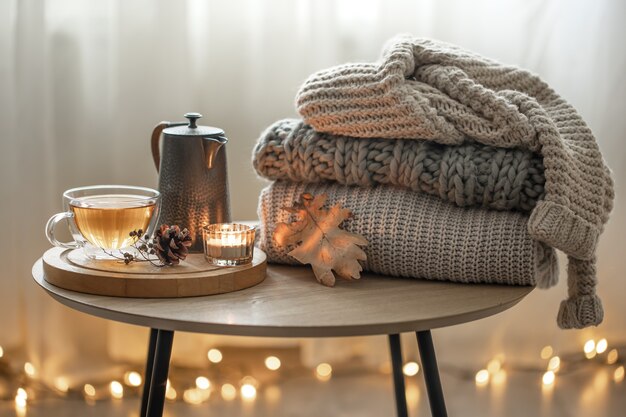 Composition d'automne à la maison avec du thé et des pulls tricotés à l'intérieur de la pièce, sur un arrière-plan flou avec une guirlande.