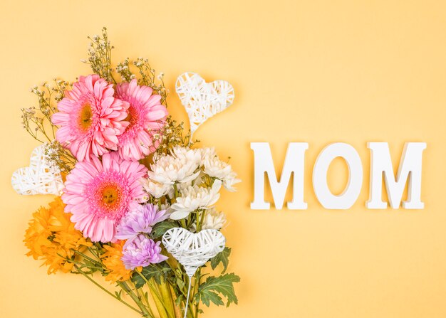 Composition de bouquet de fleurs fraîches près de coeurs d&#39;ornement sur baguettes et mot de maman