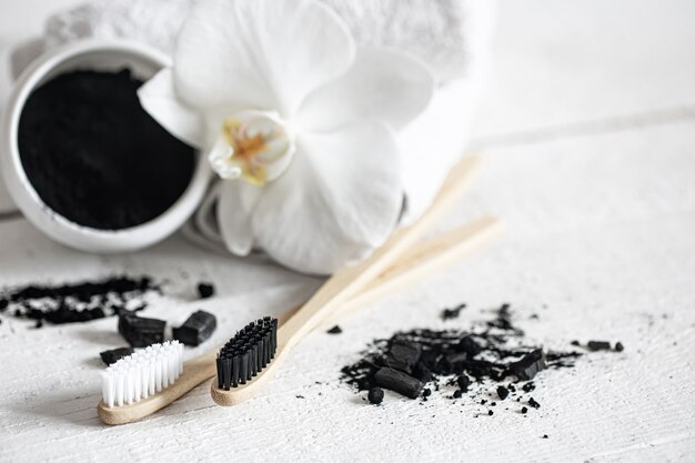 Composition avec une brosse à dents naturelle en bois, une poudre de blanchiment des dents noire et un espace de copie de fleur d'orchidée.