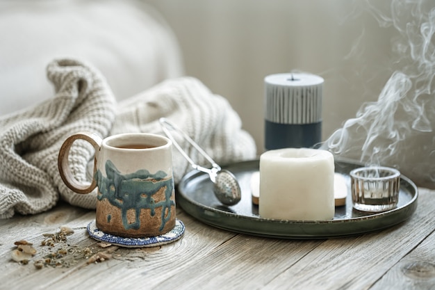 Composition confortable avec une tasse en céramique, des bougies et un élément tricoté