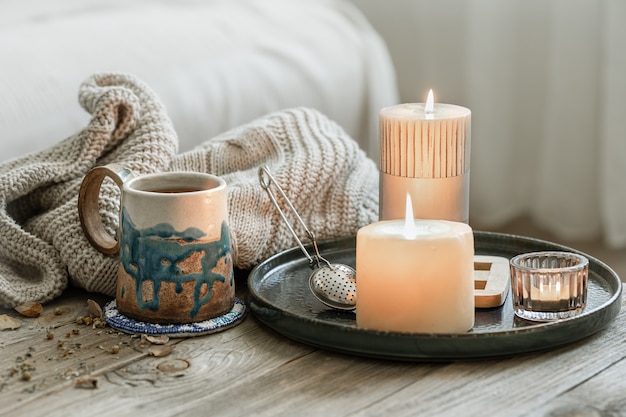 Composition confortable avec une tasse en céramique, des bougies et un élément tricoté