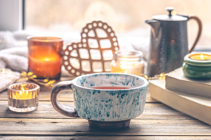 Photo gratuit composition confortable avec une tasse de thé, un livre et des bougies près de la fenêtre
