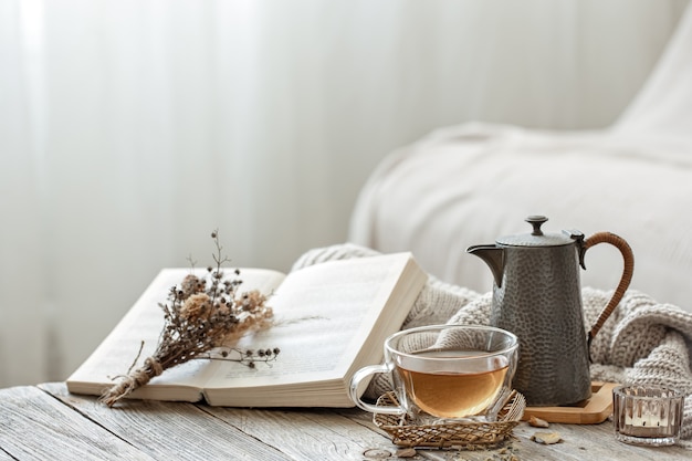 Composition confortable avec une tasse de thé et un livre à l'intérieur de la pièce sur fond flou.