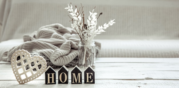 Composition dans le style hygge avec le mot en bois home, des détails de décoration et un élément tricoté