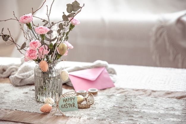 Composition festive Joyeuses Pâques avec des fleurs dans un vase en verre et des détails de décoration sur l'espace de copie de table