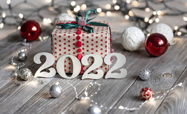 Composition festive de Noël avec numéros en bois 2022, coffret cadeau et boules de Noël sur fond flou avec bokeh.