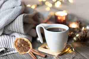 Photo gratuite composition d'hiver à la maison confortable avec une tasse de thé sur un arrière-plan flou avec des bougies allumées et des lumières bokeh et des éléments tricotés.