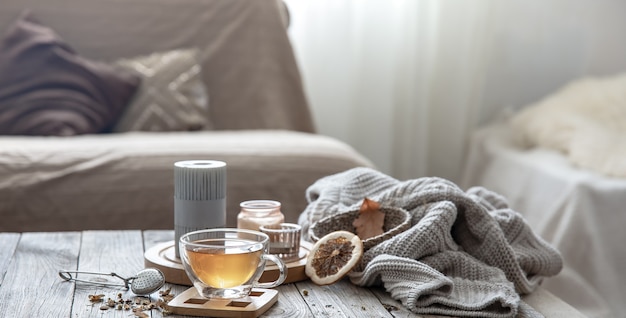 Composition de maison d'automne confortable avec une tasse de thé, des bougies et un élément tricoté sur un arrière-plan flou de l'intérieur de la pièce.