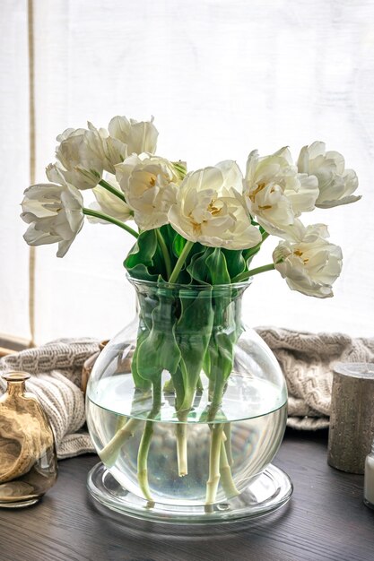 Composition maison avec un bouquet de tulipes dans un vase en verre et des bougies