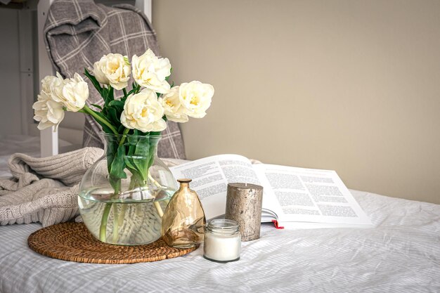 Composition maison avec un bouquet de tulipes dans un vase en verre et des bougies