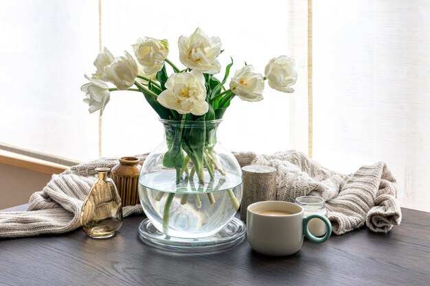 Composition maison avec un bouquet de tulipes dans un vase en verre et des bougies