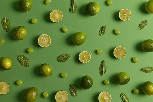 Composition à plat de limes juteuses fraîches, feuilles de menthe et raisins isolés sur fond vert. Fruits tropicaux pleins de vitamines. Ingrédients du mojito ou de la limonade. Modèle alimentaire avec agrumes