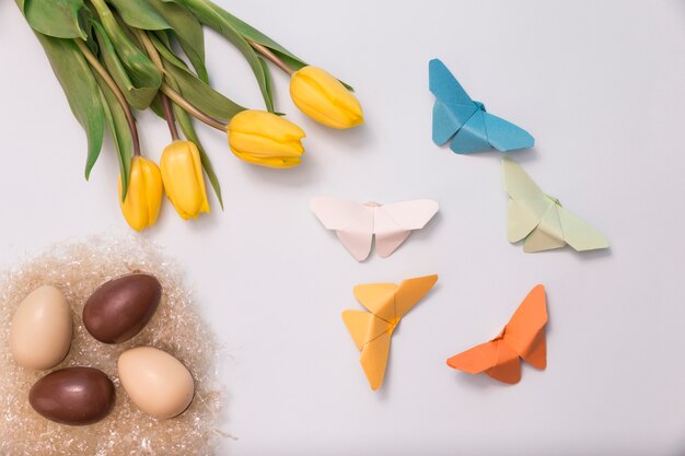 Composition de printemps avec des œufs en chocolat, les tulipes et les papillons de papier