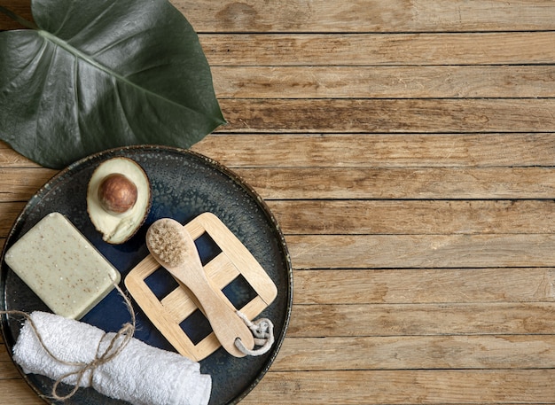 Photo gratuite composition de spa avec du savon, une serviette d'avocat, une brosse et des feuilles sur l'espace de copie de surface en bois.