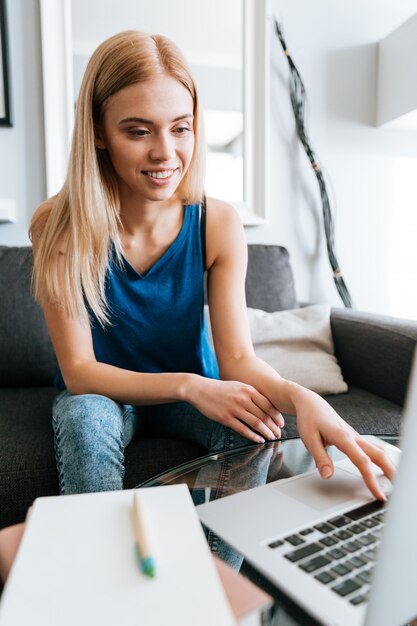 Concentré femme écrivant dans le bloc-notes et utilisant un ordinateur portable à la maison