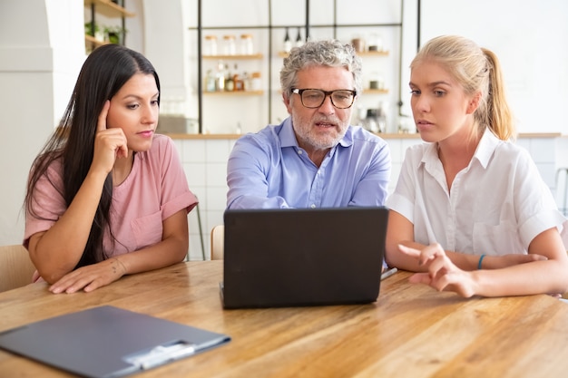 Concentré jeune femme pensive et homme mûr rencontre avec une femme professionnelle, regarder et discuter de contenu sur ordinateur portable