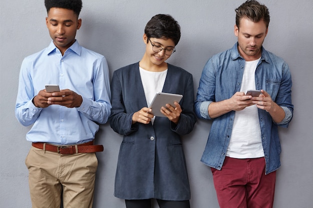 Concentré les jeunes à la mode de différentes nations, lisez attentivement les informations sur les tablettes et les téléphones intelligents