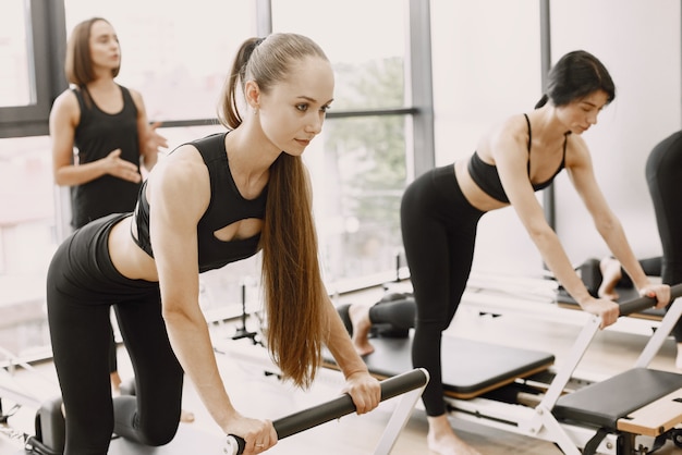 Concentrez-vous sur la femme avec une queue de cheval. Trois jeunes femmes en forme s'entraînant dans une salle de sport avec un entraîneur féminin. Femmes portant des vêtements de sport noirs.