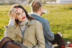 Photo gratuite concentrez-vous sur une femme qui regarde la caméra. couple romantique en vêtements de mode assis sur une nature sur un tapis de pique-nique