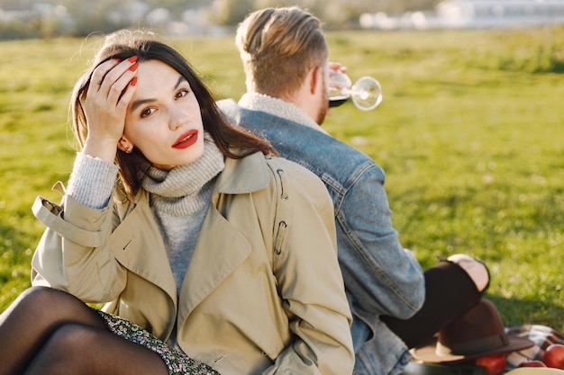 Concentrez-vous sur une femme qui regarde la caméra. Couple romantique en vêtements de mode assis sur une nature sur un tapis de pique-nique