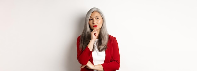 Photo gratuite concept d'affaires senior asian businesswoman réfléchie à la pensée de côté en se tenant debout sur wh