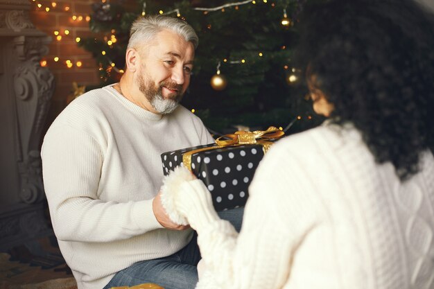 Concept D'âge Et De Personnes. Couple De Personnes âgées Avec Boîte-cadeau Sur Fond De Lumières. Femme Dans Un Sweatre Tricoté Blanc.