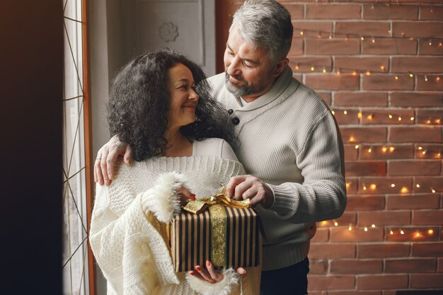 Concept d'âge et de personnes. Couple de personnes âgées avec boîte-cadeau sur fond de lumières. Femme dans un sweatre tricoté blanc.