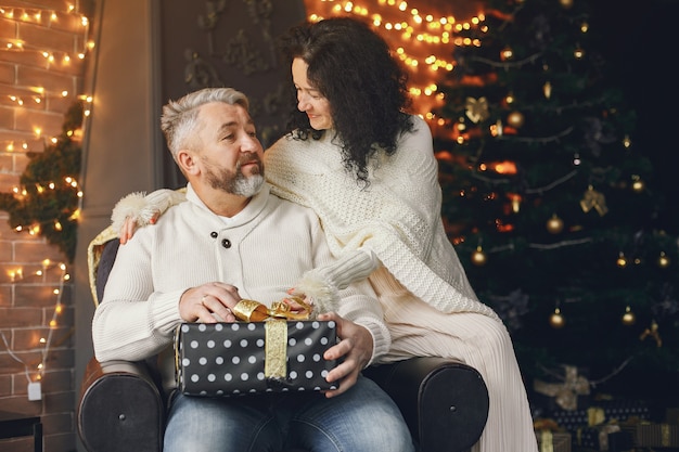 Concept d'âge et de personnes. Couple de personnes âgées avec boîte-cadeau sur fond de lumières. Femme dans un sweatre tricoté blanc.