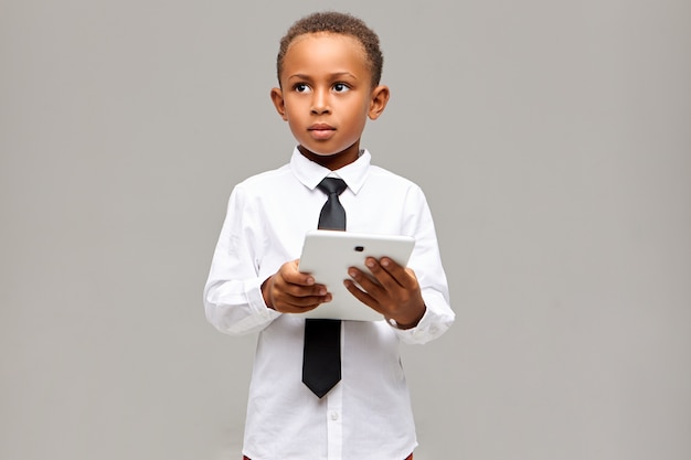 Concept d'apprentissage, d'éducation, de technologie et de communication. Bel étudiant africain intelligent en uniforme scolaire posant avec tablette tactile numérique, utilisant une connexion Internet sans fil