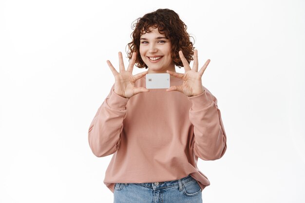 Concept bancaire et financier. Une belle fille tient et montre une carte de crédit, sourit heureusement, fait l'annonce d'une nouvelle fonctionnalité bancaire