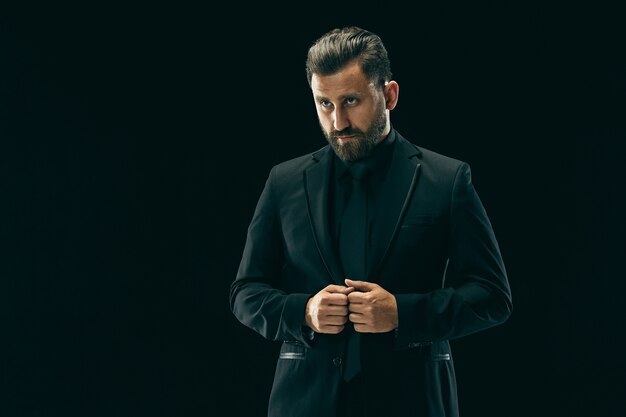 Concept de beauté masculine. Portrait d'un jeune homme à la mode avec une coupe de cheveux élégante portant un costume tendance posant sur fond noir.