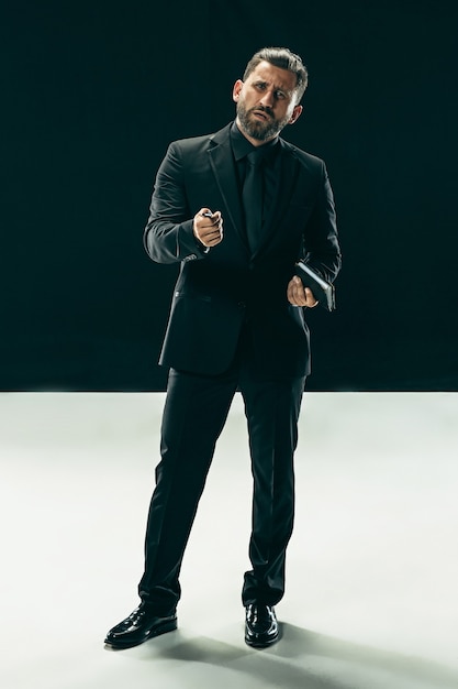 Concept de beauté masculine. Portrait d'un jeune homme à la mode avec une coupe de cheveux élégante portant un costume tendance posant sur un mur noir.