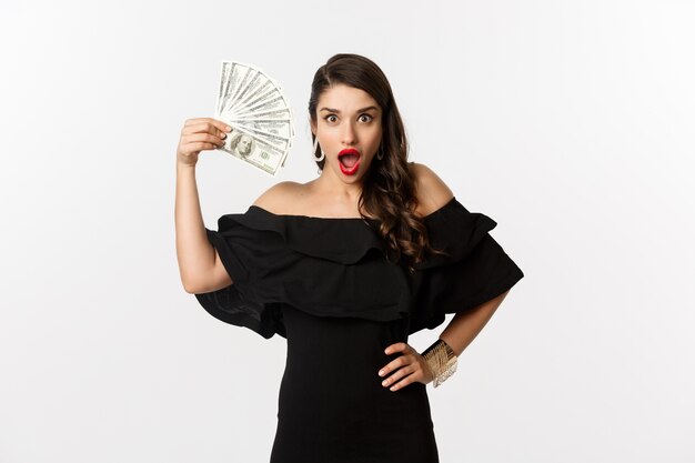 Concept de beauté et de shopping. Femme à la mode avec des lèvres rouges, montrant des dollars et souriant, debout sur fond blanc avec de l'argent.