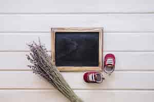 Photo gratuite concept de bébé avec ardoise, branches et chaussures sur la surface en bois