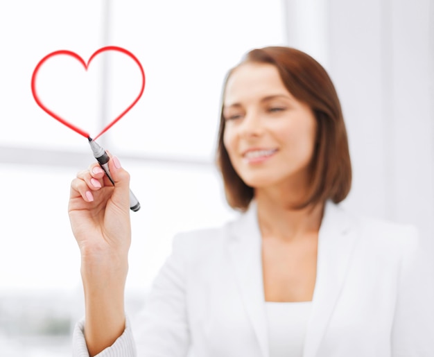 Concept de bureau, d'entreprise et de technologie - femme d'affaires dessinant un coeur en l'air avec un marqueur