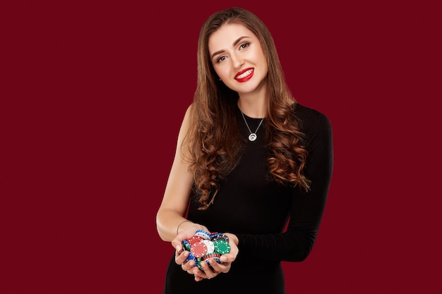 Concept de casino, de jeu, de poker, de personnes et de divertissement - joueur de poker femme en robe noire avec des jetons dans les mains sur fond rouge.