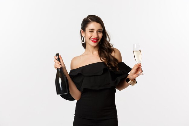 Concept de célébration et de fête. Femme brune élégante en robe glamour tenant une bouteille et une coupe de champagne, s'amusant pendant les vacances du nouvel an.