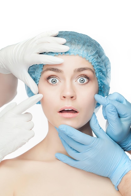 Concept de chirurgie plastique. Mains de docteur dans des gants touchant le beau visage de femme sur le blanc