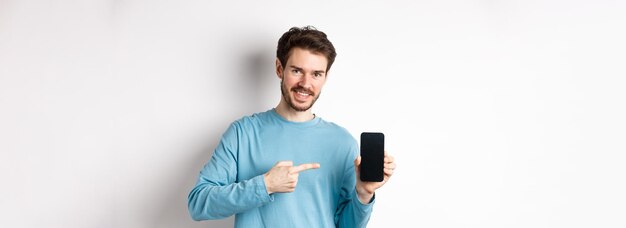 Concept de commerce électronique et de shopping homme caucasien souriant pointant du doigt le spectacle d'écran de smartphone vide