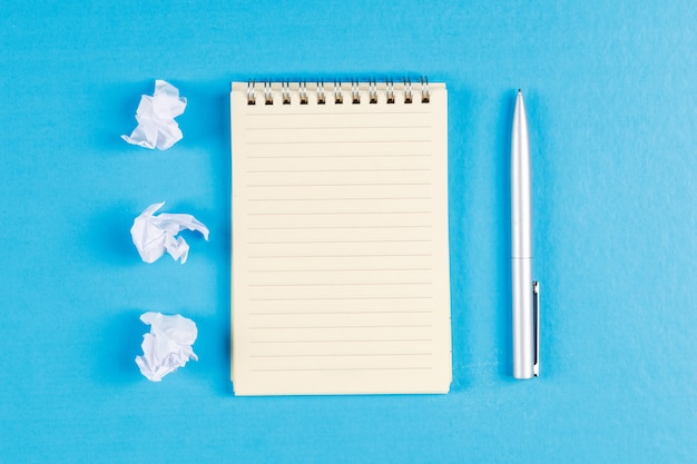 Concept commercial et financier avec des liasses de papier froissé, cahier à spirale, stylo sur fond plat bleu.