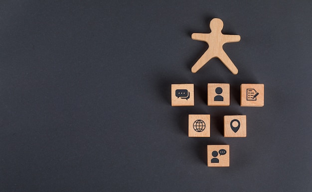 Concept de communication avec des icônes sur des cubes en bois, figure humaine sur table gris foncé à plat.