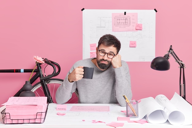 Concept de construction et d'architecture d'ingénierie. Un employé de bureau fatigué boit un café rafraîchissant travaille toute la nuit à une tâche urgente a une date limite pour terminer le travail pose au bureau dans un espace de coworking.