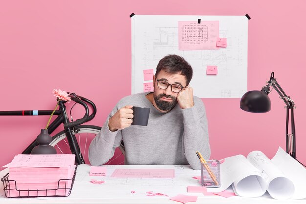 Concept de construction et d'architecture d'ingénierie. Un employé de bureau fatigué boit un café rafraîchissant travaille toute la nuit à une tâche urgente a une date limite pour terminer le travail pose au bureau dans un espace de coworking.